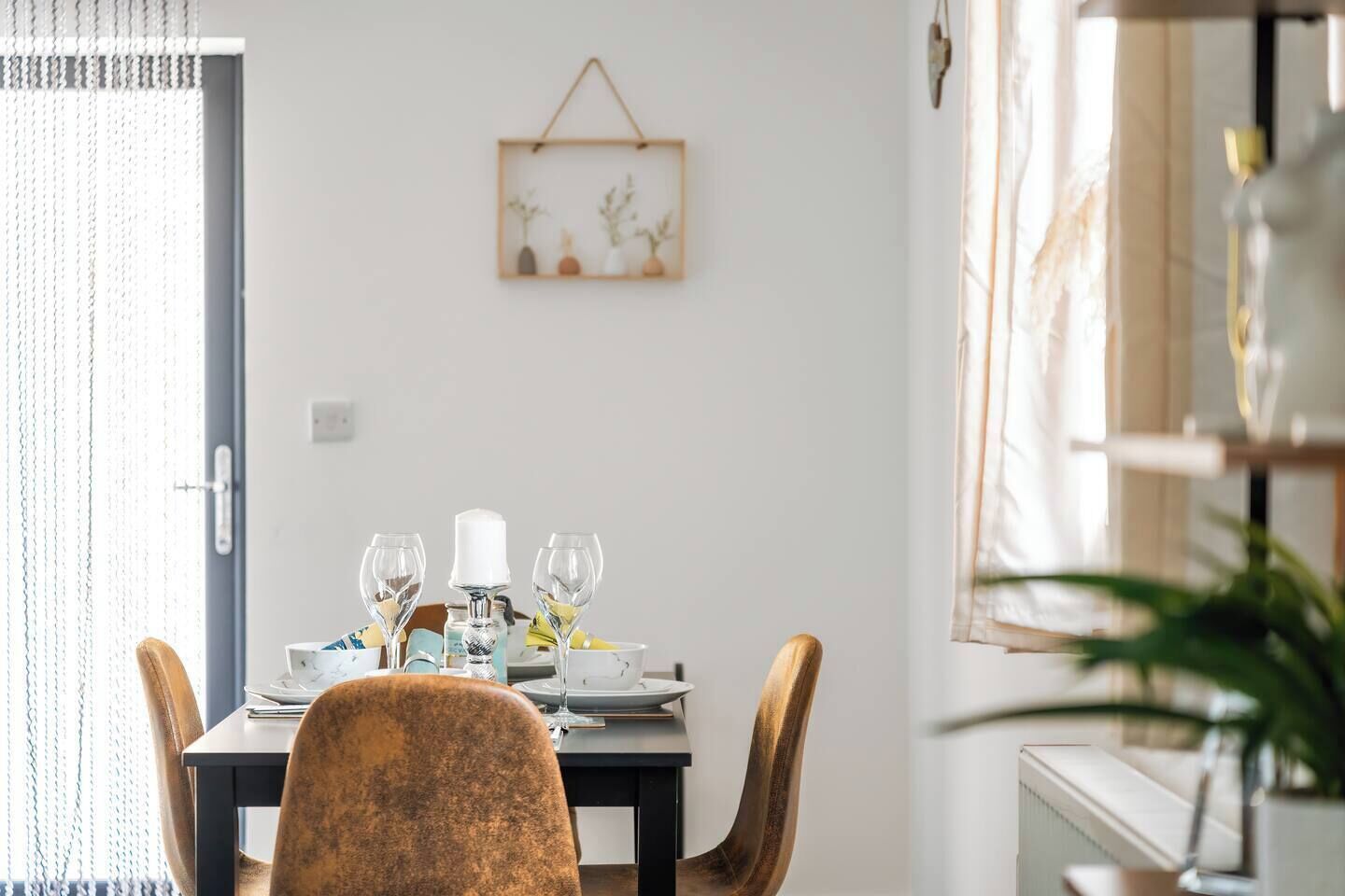 A dining area with a table set for four, a hanging plant, and a window with curtains.