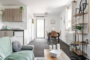 A modern living room with a sofa, a dining area with a table and chairs, and a kitchen with cabinets and a refrigerator. - Modern 1-Bed Apartment with Parking near Heathrow (Slough)