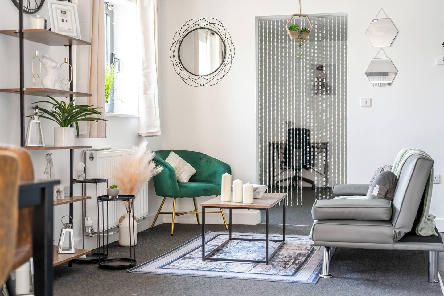 Un salon moderne avec un fauteuil vert, un canapé gris, une table basse ornée de bougies et un miroir décoratif.