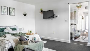 A bedroom with a bed, a TV mounted on the wall, and a sliding glass door leading to a balcony. - Modern 1-Bed Apartment with Parking near Heathrow (Slough)