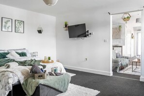 Un dormitorio con cama, televisor montado en la pared y puerta corrediza de vidrio que da a un balcón.