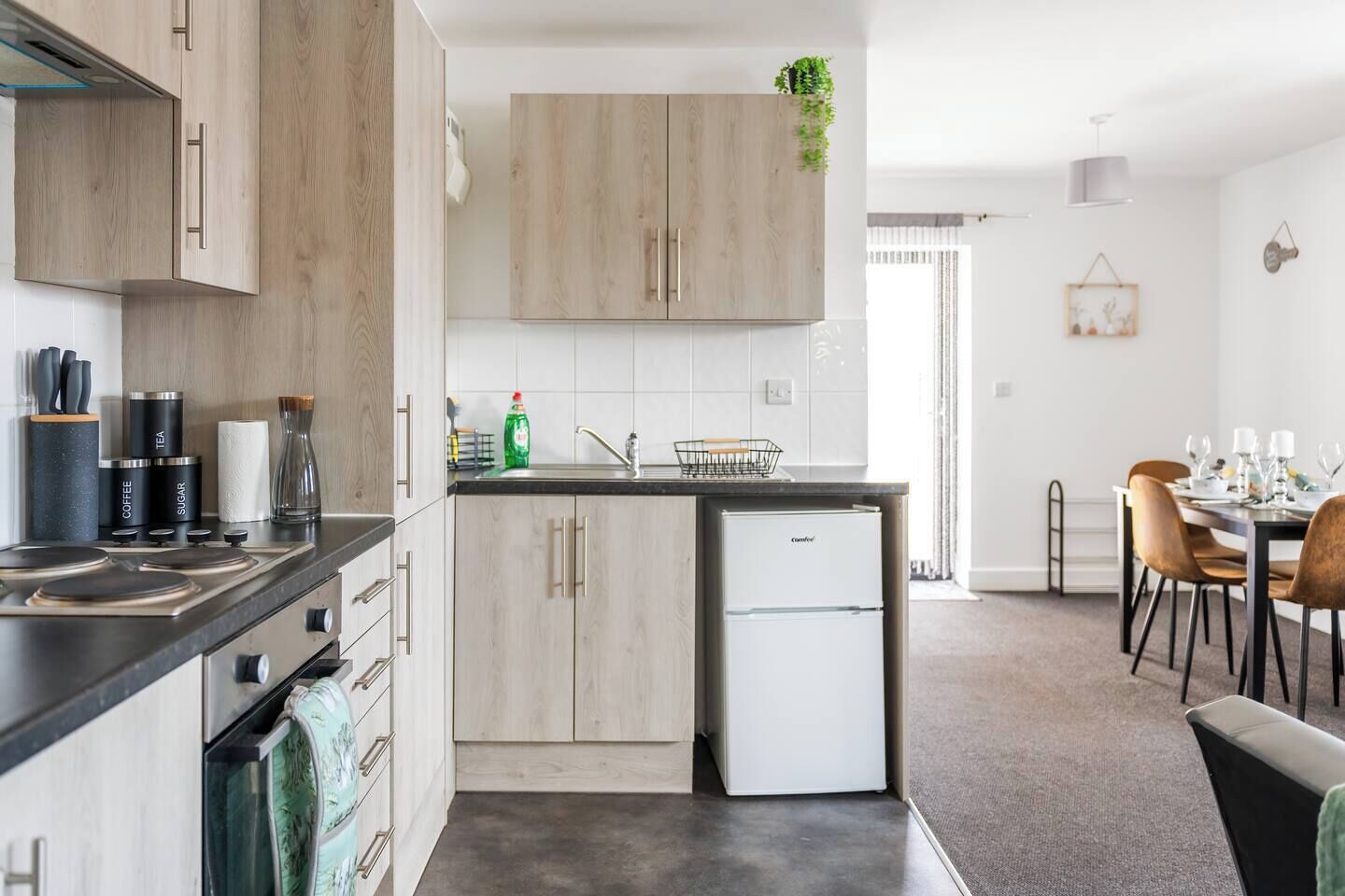 Ett modernt kök med träskåp, en inbyggd diskmaskin och en matplats med ett bord för fyra personer.