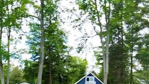 En träbrygga som sträcker sig ut i vattnet, med ett hus i bakgrunden.