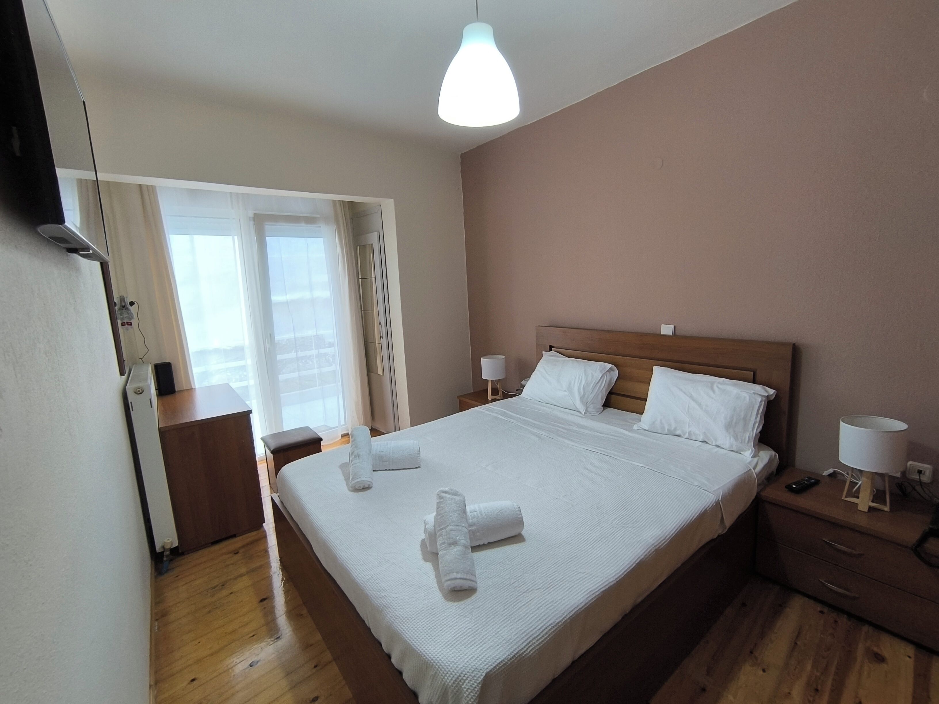 Una habitación de hotel con una cama grande, mesitas de noche, un armario y una ventana con cortinas.