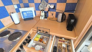 Une cuisine compacte équipée d’une cuisinière, d’une machine à café et d’un organiseur de tiroir contenant des ustensiles.