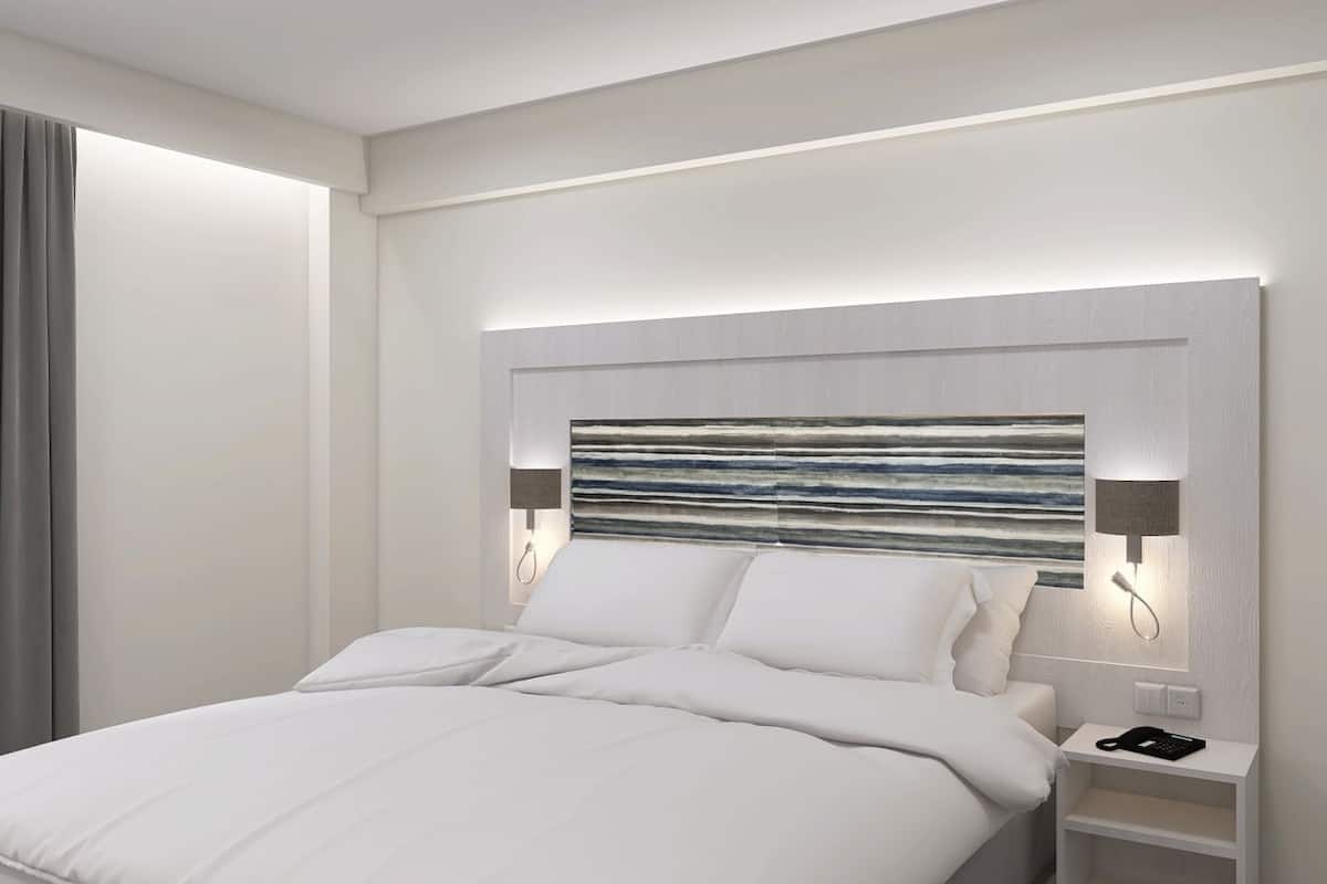 A modern hotel room with a large bed, a headboard with a textured design, bedside lamps, and a telephone on the nightstand.