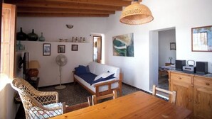 A cozy room with a wooden dining table, a wicker chair, a sofa, a fan, and a painting on the wall. - Rural House Ca Ses Llussianes - ET/0641 (Sant Francesc de Formentera)