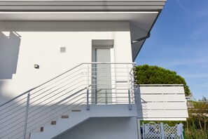 Un edificio moderno con fachada blanca, puerta de cristal y una escalera metálica que conduce a un balcón con plantas.