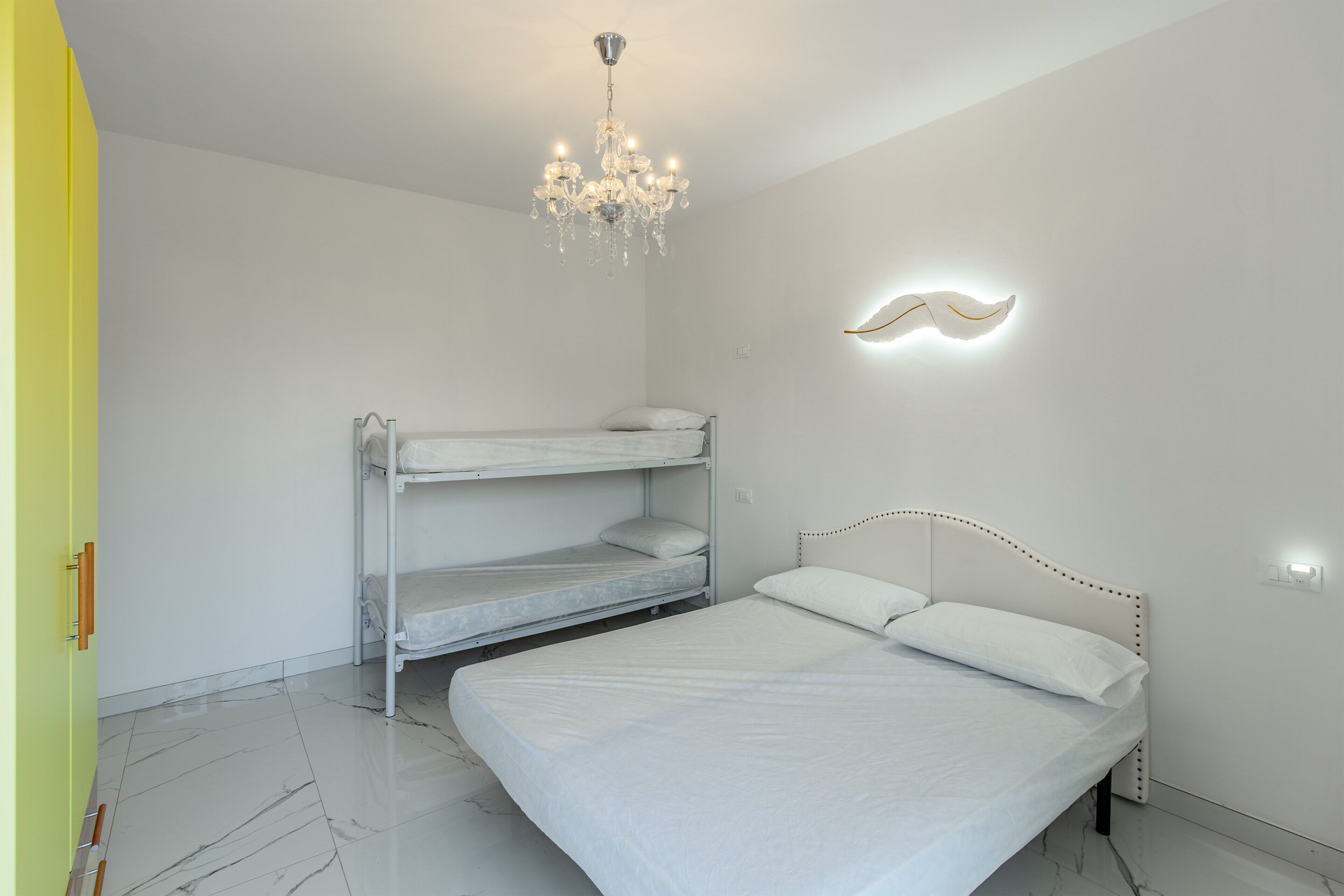 Un dormitorio con una cama litera, una cama individual, una araña y un aplique de pared.