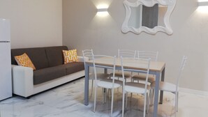 A dining area with a table and chairs, a sofa with cushions, a wall-mounted mirror, and a light fixture. - Apartment 'Teresa' with Shared Pool, Private Terrace and Air Conditioning (Bibione)