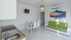 A modern living space with a dining area, a green sofa, a TV, and a painting of a sunset. - Apartment 'Teresa' with Shared Pool, Private Terrace and Air Conditioning (Bibione)