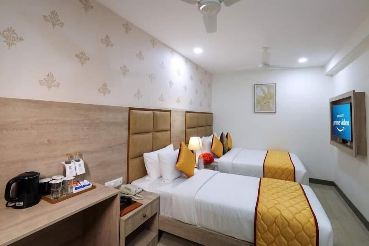 A hotel room with two beds, a desk with a coffee maker, a phone, and a television displaying the Prime Video logo.