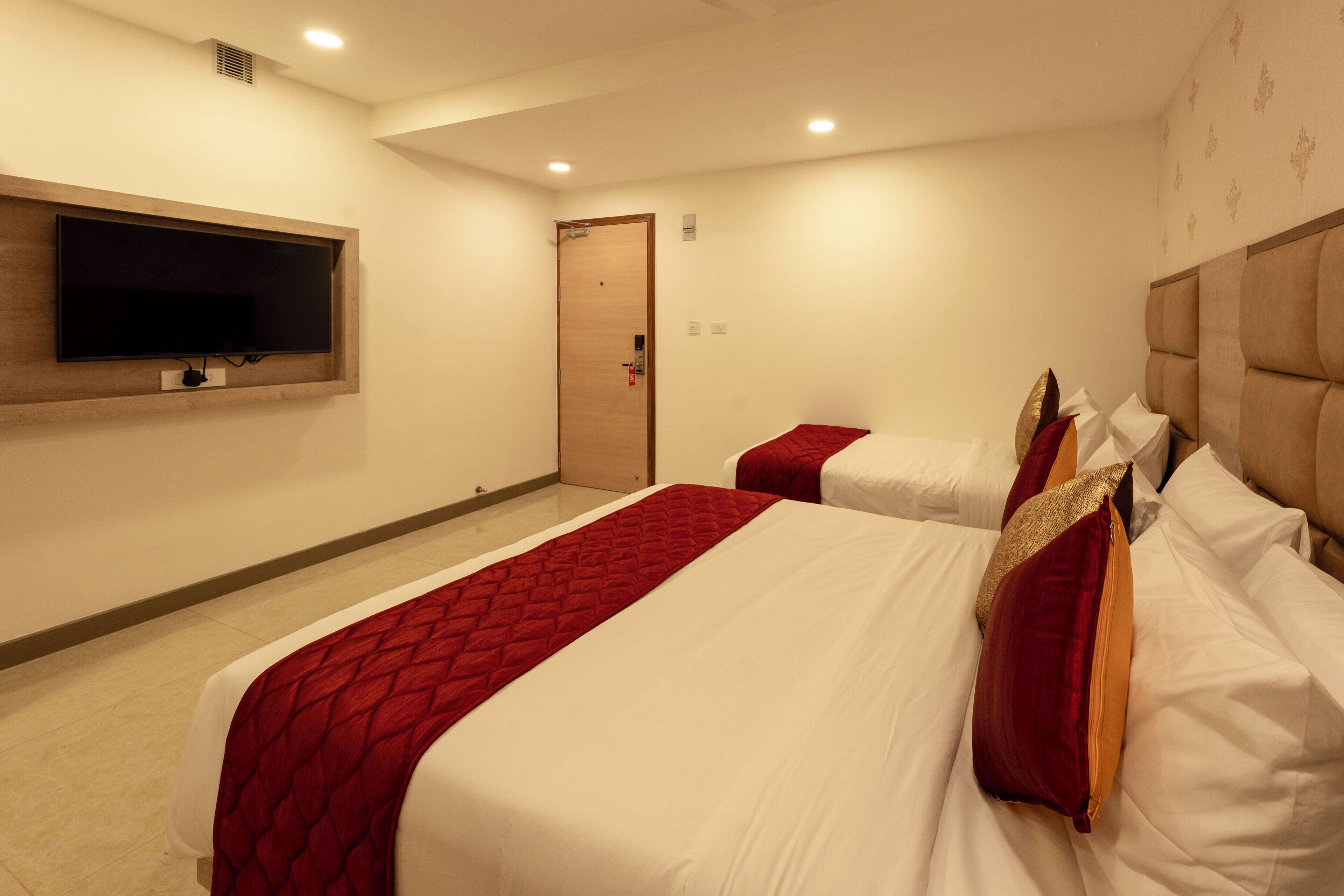 Una habitación de hotel con dos camas, un televisor montado en la pared y una puerta.