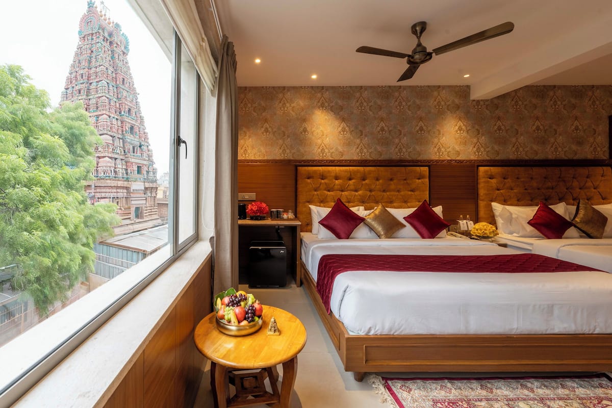 A hotel room with a large bed, a ceiling fan, and a view of a temple through the window.