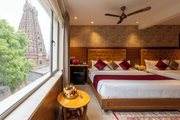 A hotel room with a large bed, a ceiling fan, and a view of a temple through the window.