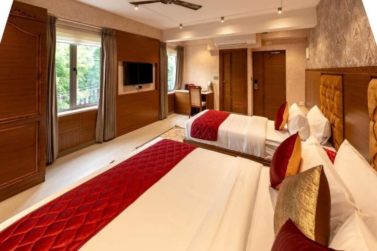 A hotel room with two beds, a TV, a desk, and a window with curtains.
