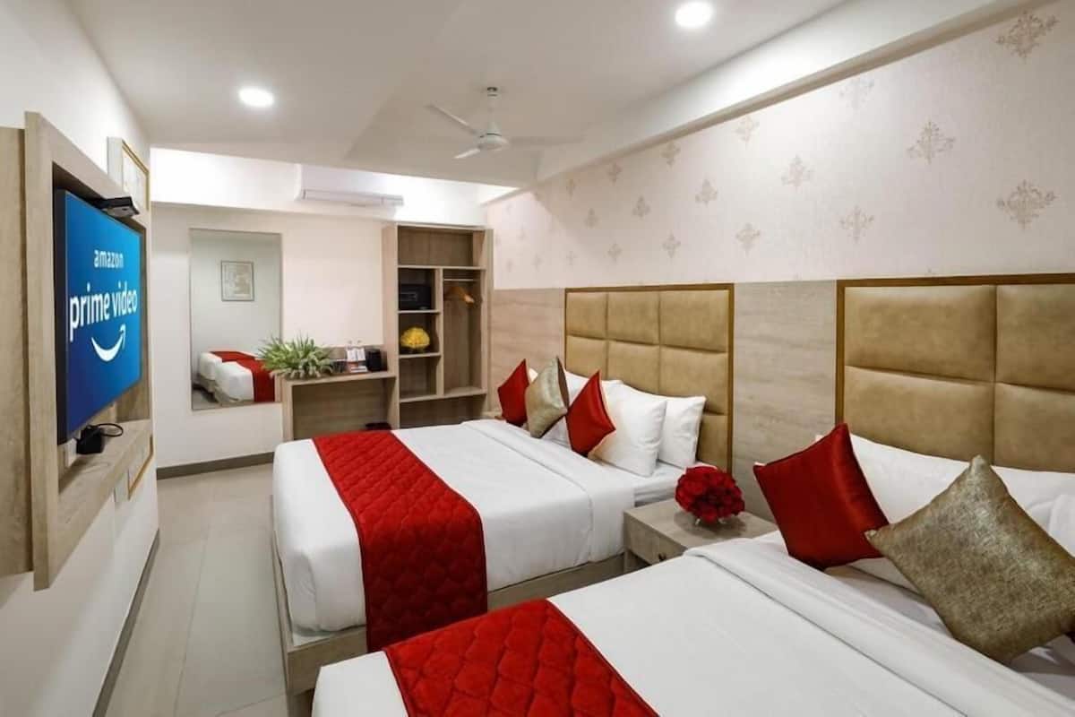 A hotel room with two beds, a TV displaying Amazon Prime Video, a ceiling fan, and a small seating area with a plant.