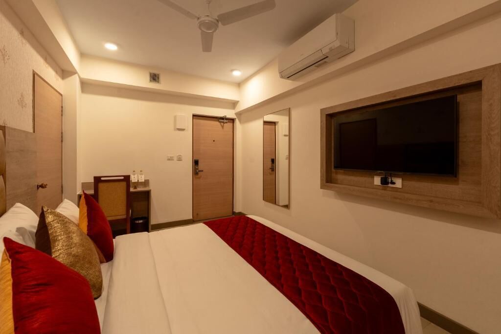A hotel room with a bed, a TV, an air conditioning unit, and a ceiling fan.