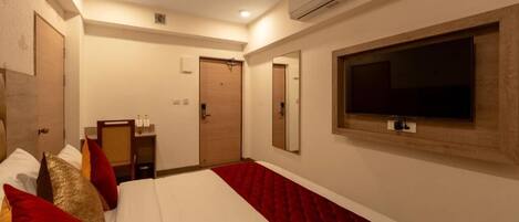 Una habitación de hotel con cama, televisión, aire acondicionado y ventilador de techo.