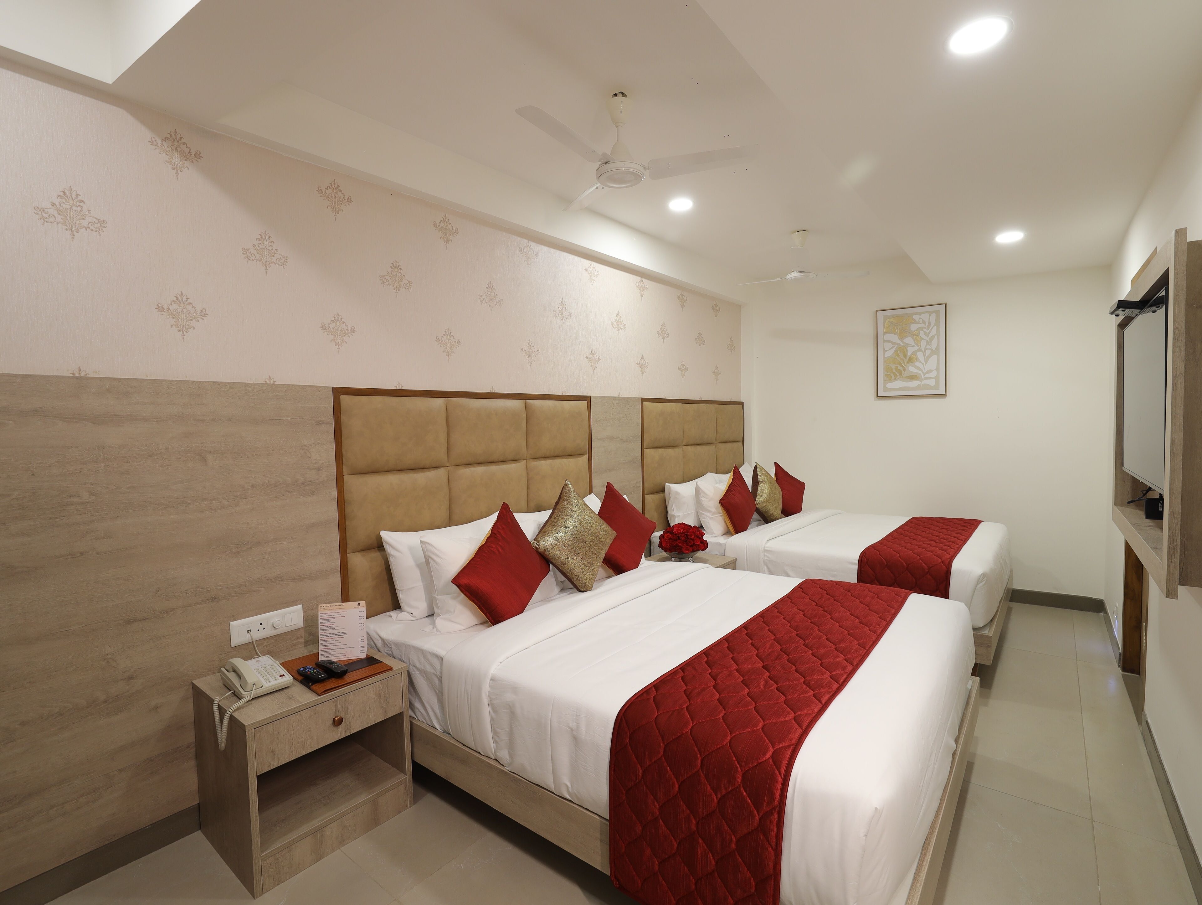 A hotel room with two beds, a wooden headboard, a nightstand with a phone, and a ceiling fan.