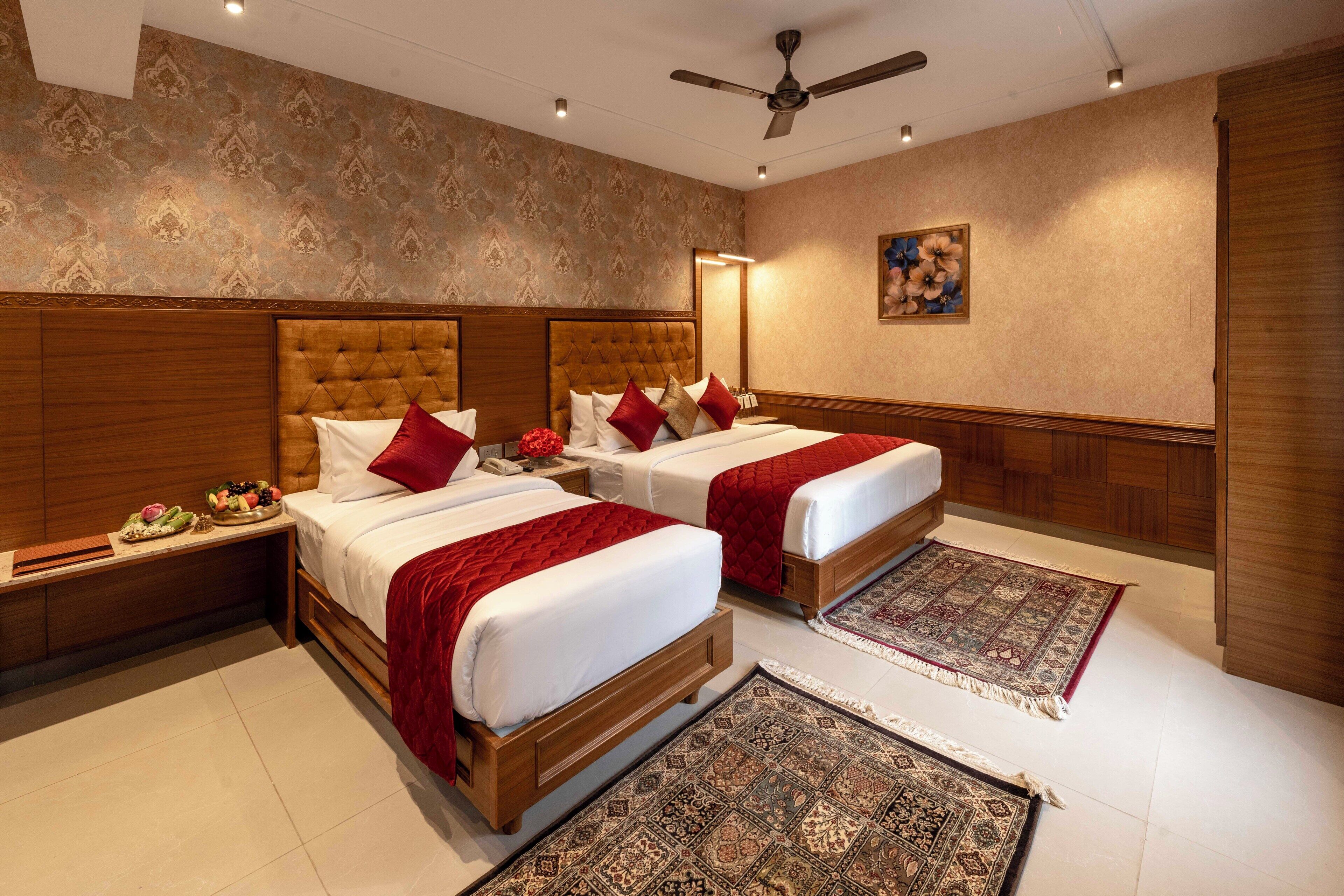 A hotel room with two beds, a ceiling fan, a large mirror, and a decorative rug.