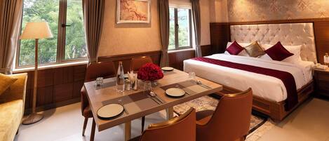 Une chambre d’hôtel avec un grand lit, une table à manger avec des chaises, un ventilateur de plafond et de grandes fenêtres avec des rideaux.