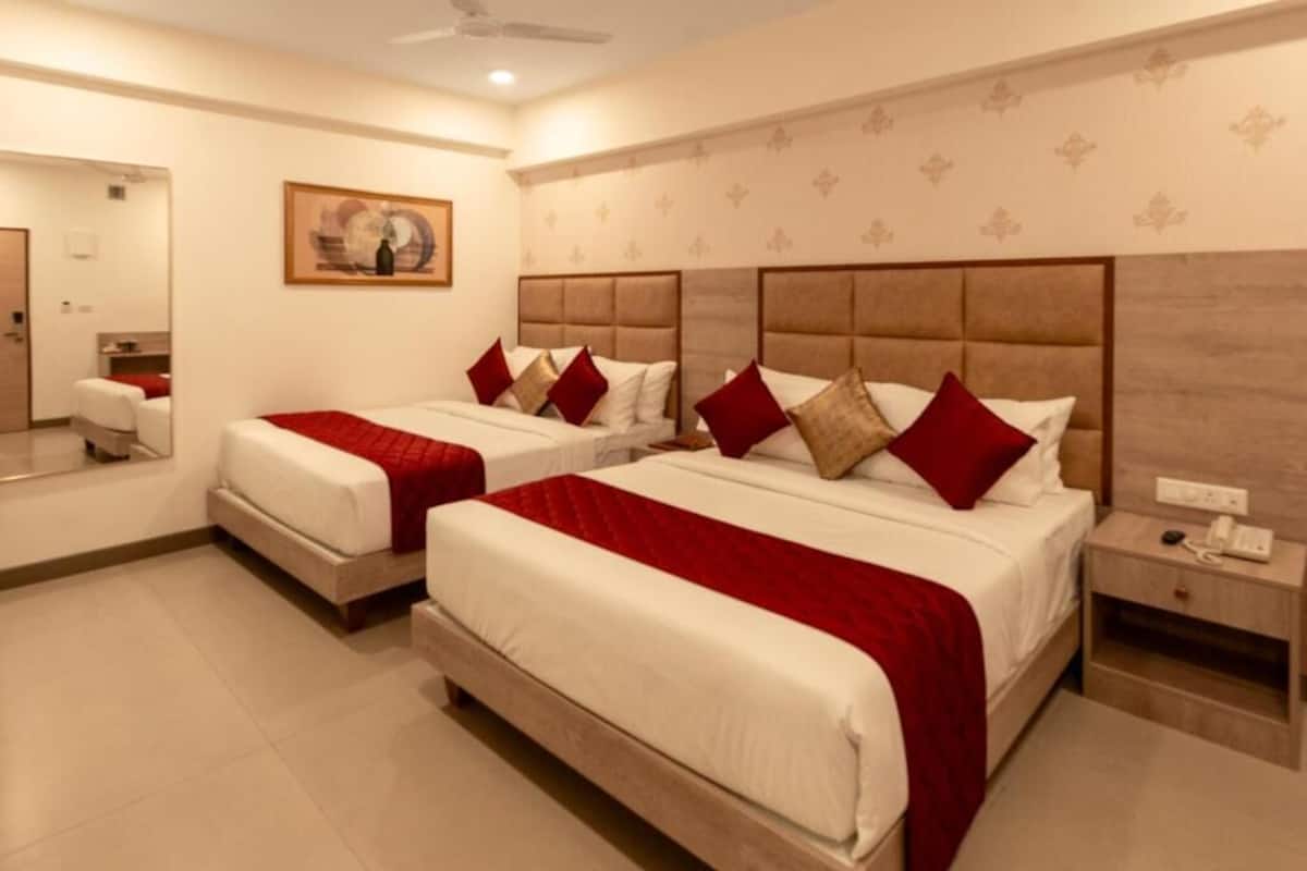 A hotel room with two beds, a bedside table with a phone, and a mirror.