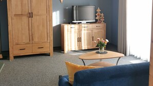 Uma sala de estar com sofá, mesa de centro com flores, TV, armários de madeira e um guarda-roupa grande.