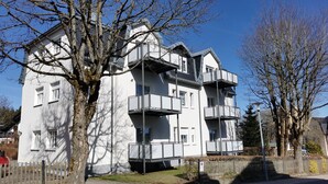 Um edifício residencial com vários andares, varandas, entrada com portão e céu claro.