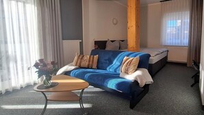 Quarto com sofá azul, mesa de madeira, cama e janela com cortinas.