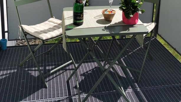 Varanda com mesa, cadeiras, uma garrafa de champanhe e um vaso de flores.