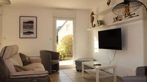 Een woonkamer met een bank, fauteuil en een aan de muur bevestigde televisie.