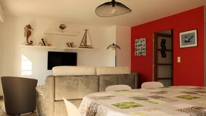 Een kamer met een slaapbank, een eettafel en een aan de muur bevestigde televisie.