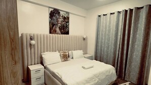 Un dormitorio moderno con una cama grande, mesitas de noche, cabecera y una lámpara en el techo.