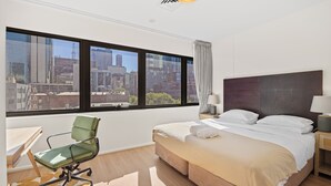 Ein Hotelzimmer mit großem Fenster, einem Bett, einem Schreibtisch und einem Stuhl.