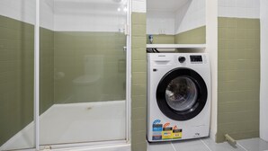Ein kleines Badezimmer mit einer Duschkabine, einer weißen Waschmaschine und grünen Fliesen.