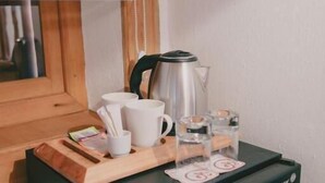 Una kitchenette compacta con cafetera, tazas, vasos y un refrigerador pequeño.