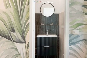Ein Badezimmer mit modernem Design, mit einem runden Spiegel über einem dunkel gefärbten Waschbecken und Schränken.