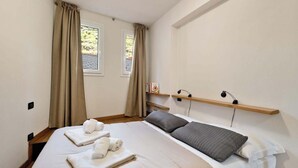 Ein Schlafzimmer mit einem Bett, zwei Nachttischen, einem Fenster mit Vorhängen und einem Regal mit Büchern.
