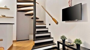 Eine moderne Treppe mit schwarzen Stufen und Holzhandläufen, ein angebrachtes Fernsehgerät und zwei Blumentöpfe auf einem Konsolentisch.