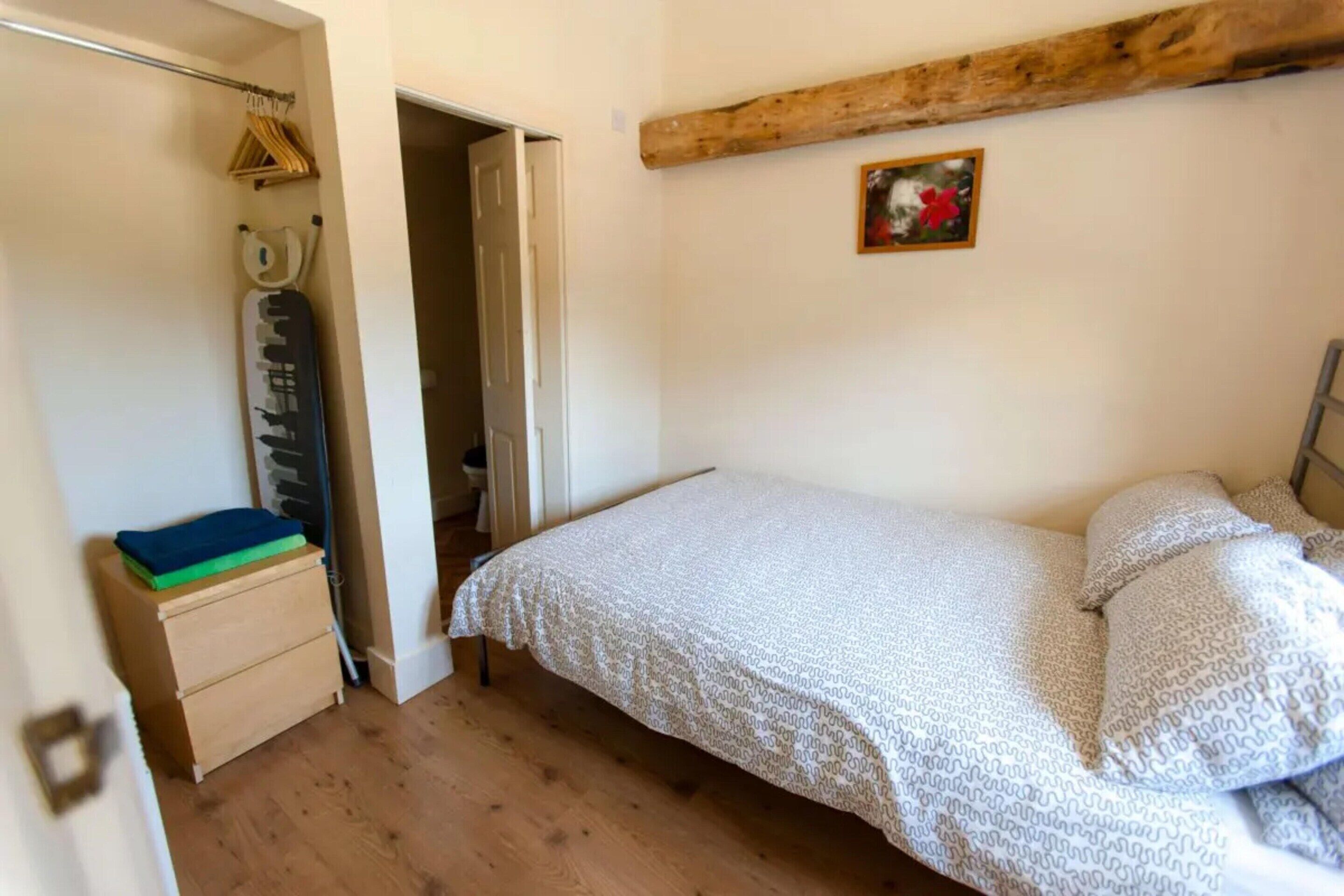 A bedroom with a bed, a wooden floor, a wardrobe, and a door leading to another room.