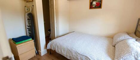 A bedroom with a bed, a wooden floor, a wardrobe, and a door leading to another room.