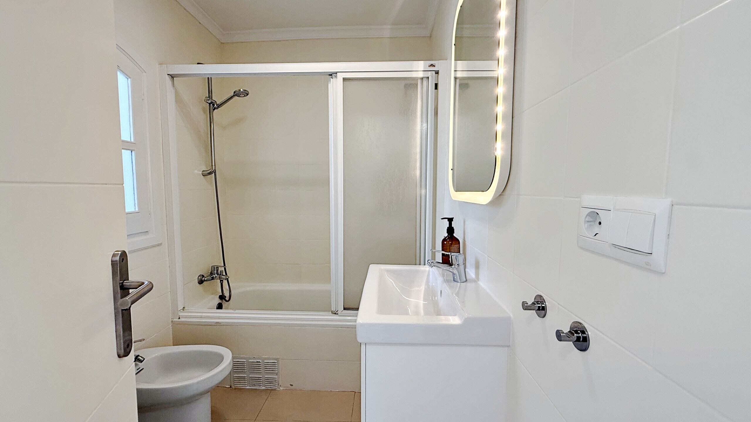 A bathroom with a shower, toilet, sink, and a mirror with lights.