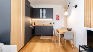 Une cuisine de taille réduite, avec des meubles de couleur sombre, un plan de travail en bois et un coin repas comprenant une table et des chaises.
