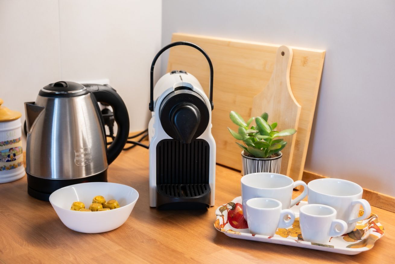 A kitchen counter with a coffee maker, a kettle, a bowl of coffee beans, and a tray with cups and a small plant.