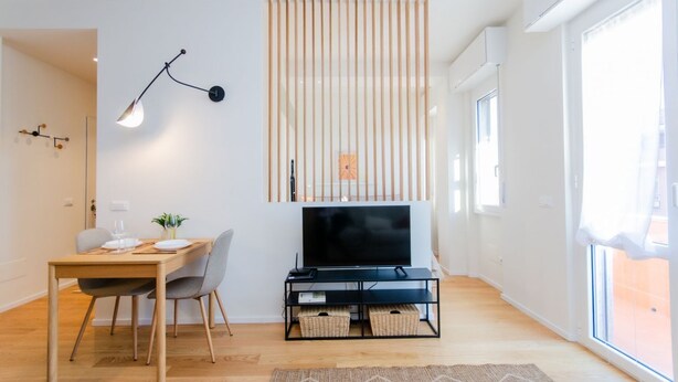 Un salon moderne avec une table à manger en bois, un meuble TV noir et une grande fenêtre.