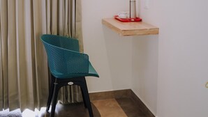 Une pièce d’angle avec un fauteuil turquoise, une étagère en bois sur laquelle se trouve un thermos et un rideau.