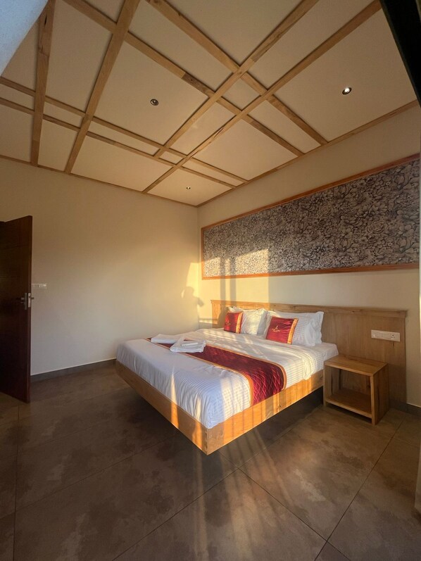 A bedroom with a wooden headboard, a large bed with white bedding and red accents, a nightstand, and a wall-mounted artwork.