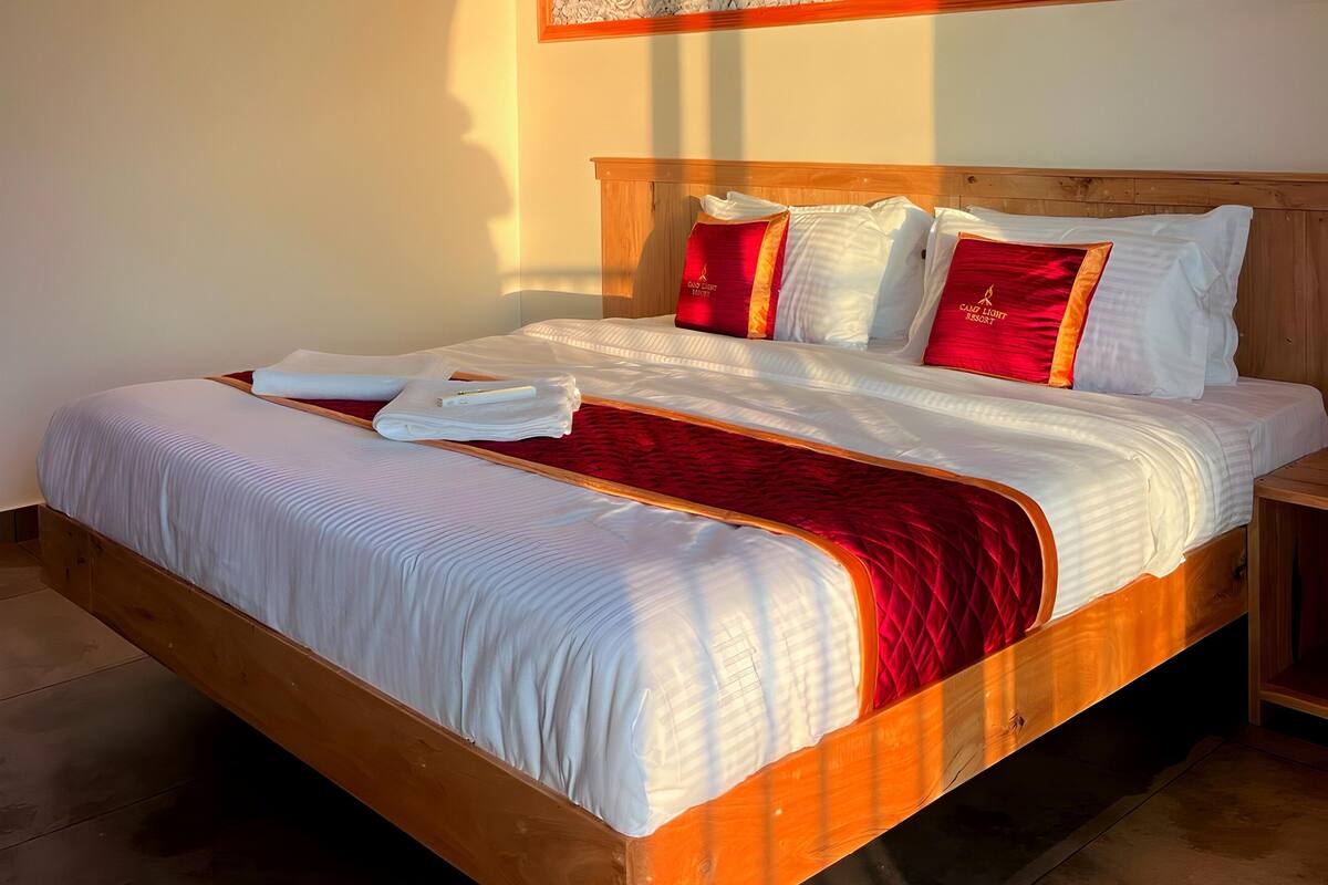 Una cama bien hecha con sábanas blancas, una colcha rayada de rojo y blanco y almohadas a juego.