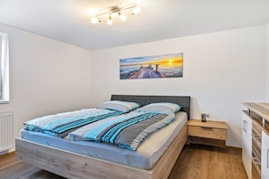 A bedroom with a bed, a nightstand, a drawer, a painting on the wall, and a window. - Apartment 'Winder' with Mountain View, Private Terrace and Wi-Fi (Lustenau)
